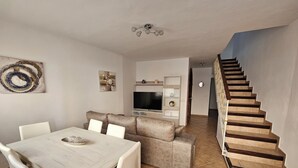 Una sala de estar moderna con comedor, una escalera y un televisor.