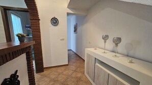 Un pasillo con un banco de madera, un reloj de pared y un aparador con cristalería decorativa.