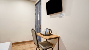 Een kleine kamer met een houten tafel, een stoel, een aan de muur bevestigde televisie en een deur.