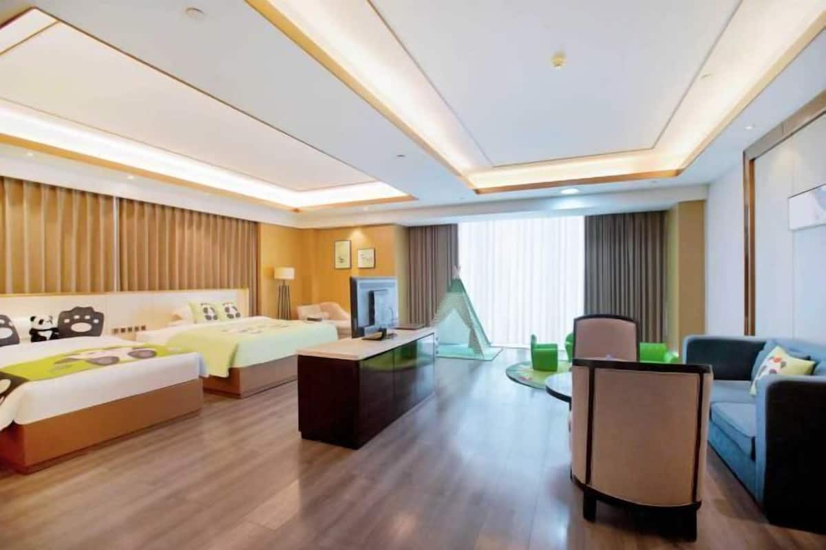 A hotel room with a bed, a desk, a chair, a sofa, and a TV.