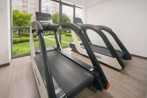 Una caminadora en un cuarto con un ventanal grande, una laptop sobre la caminadora, y vista a un jardín exterior.