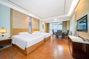 A hotel room with two beds, a desk, a chair, a television, and a bathroom.