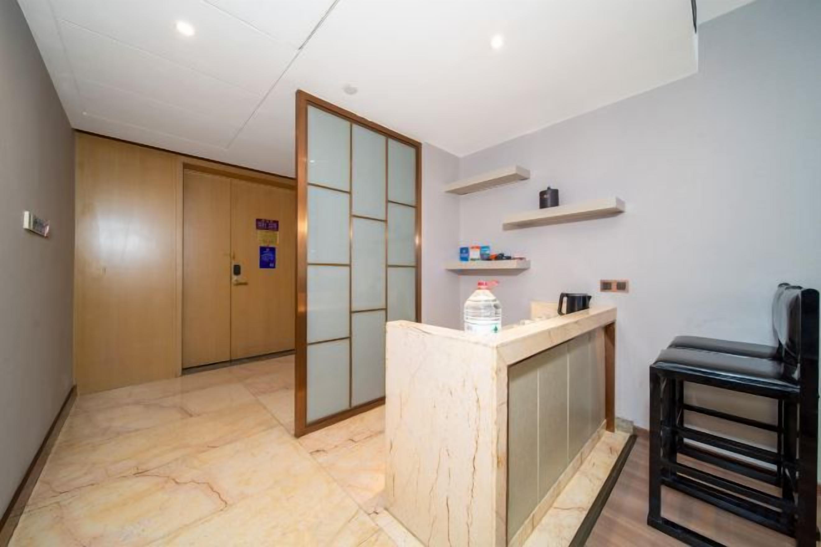 Una habitación de hotel con puerta de madera, mostrador de recepción, dispensador de agua y una silla negra.
