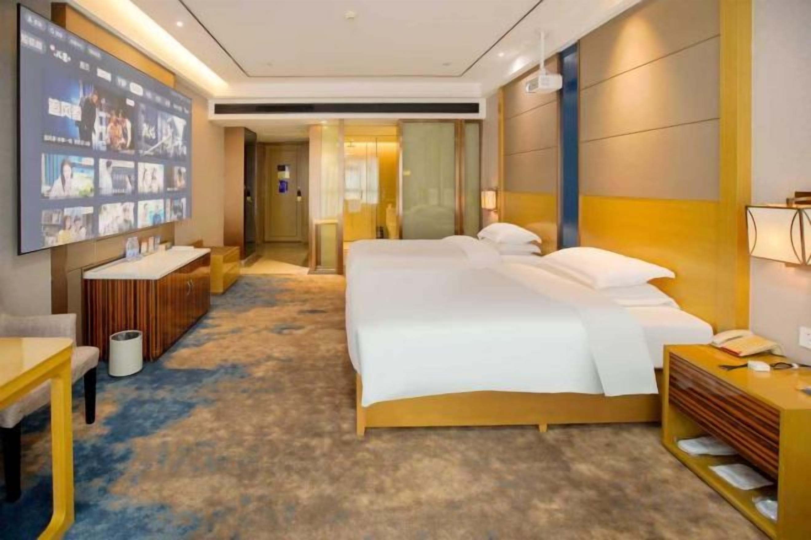 Une chambre d’hôtel avec un grand lit, un bureau, une télévision et une salle de bain visible à travers une porte ouverte.