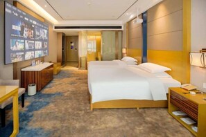 Habitación de hotel con una cama grande, un escritorio, un televisor y un baño visible a través de una puerta abierta.