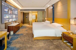 Habitación de hotel con una cama grande, un escritorio, un televisor y un baño visible a través de una puerta abierta.