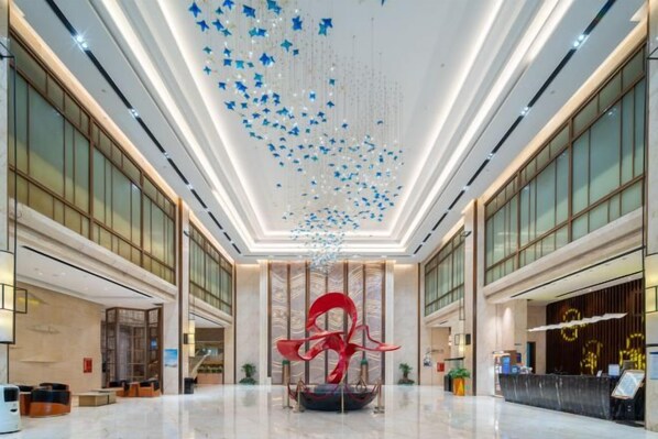Un vestíbulo espacioso con techo alto, una escultura roja central y un mostrador de recepción.