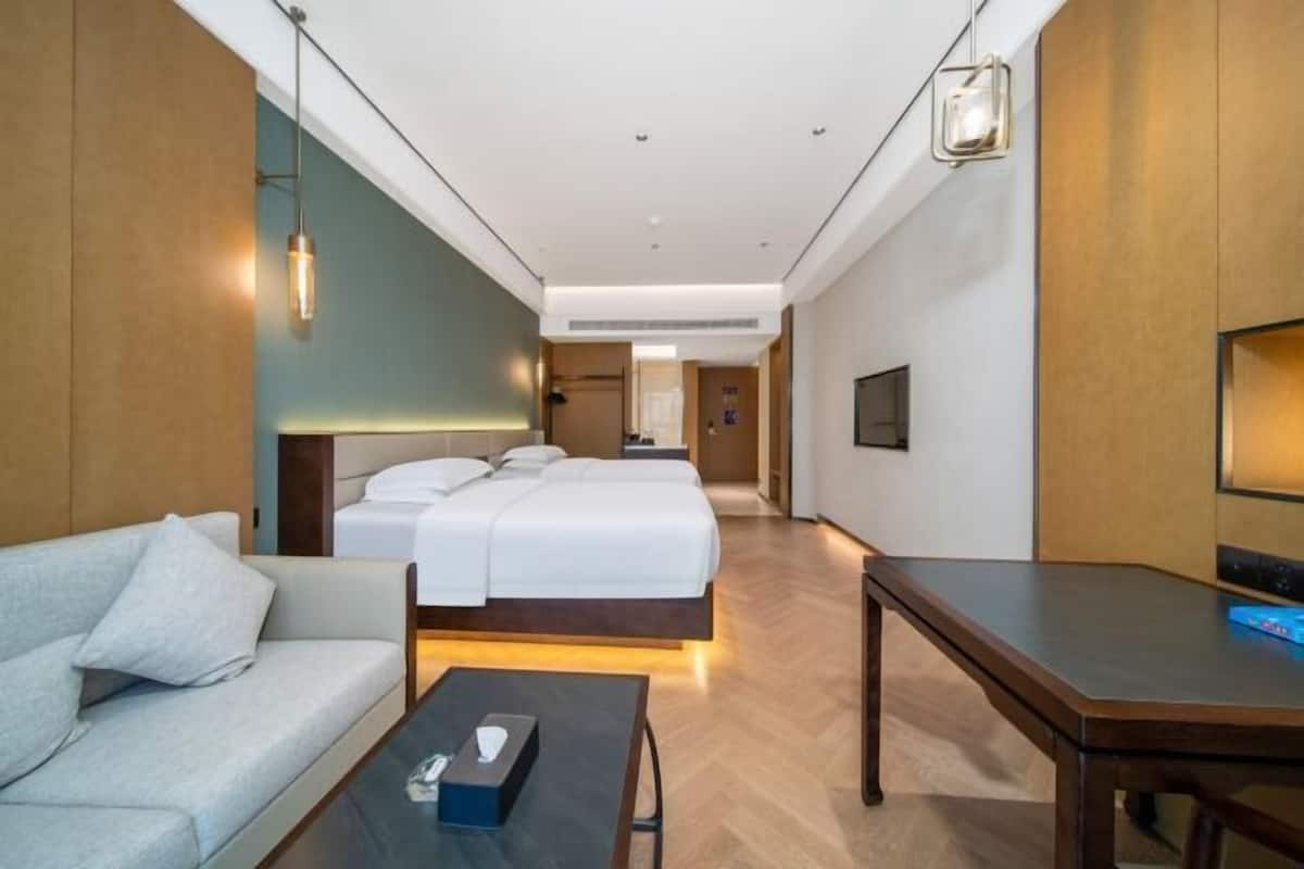 A hotel room with a sofa, a bed with white linens, a small table with a tissue box, and a TV on the wall.
