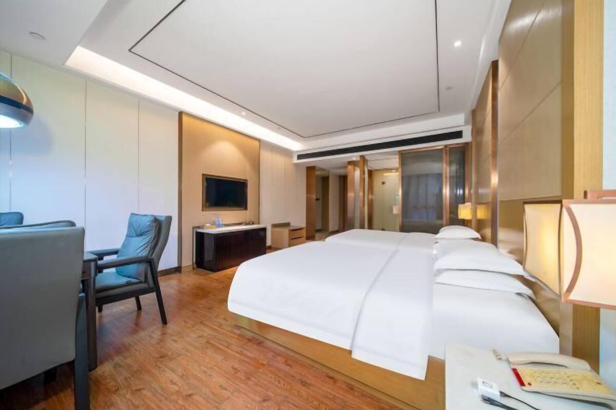 A modern hotel room with a large bed, a desk, a chair, and a TV.