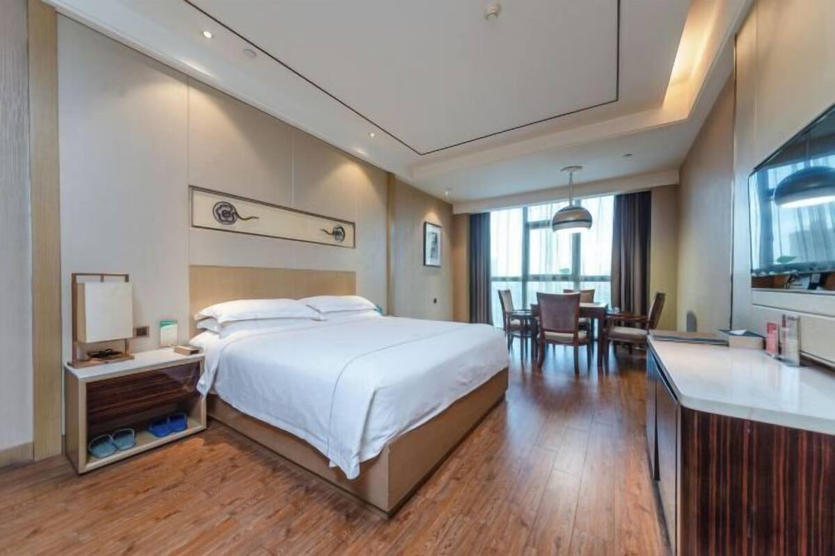 A modern hotel room with a large bed, a desk, and a dining area.