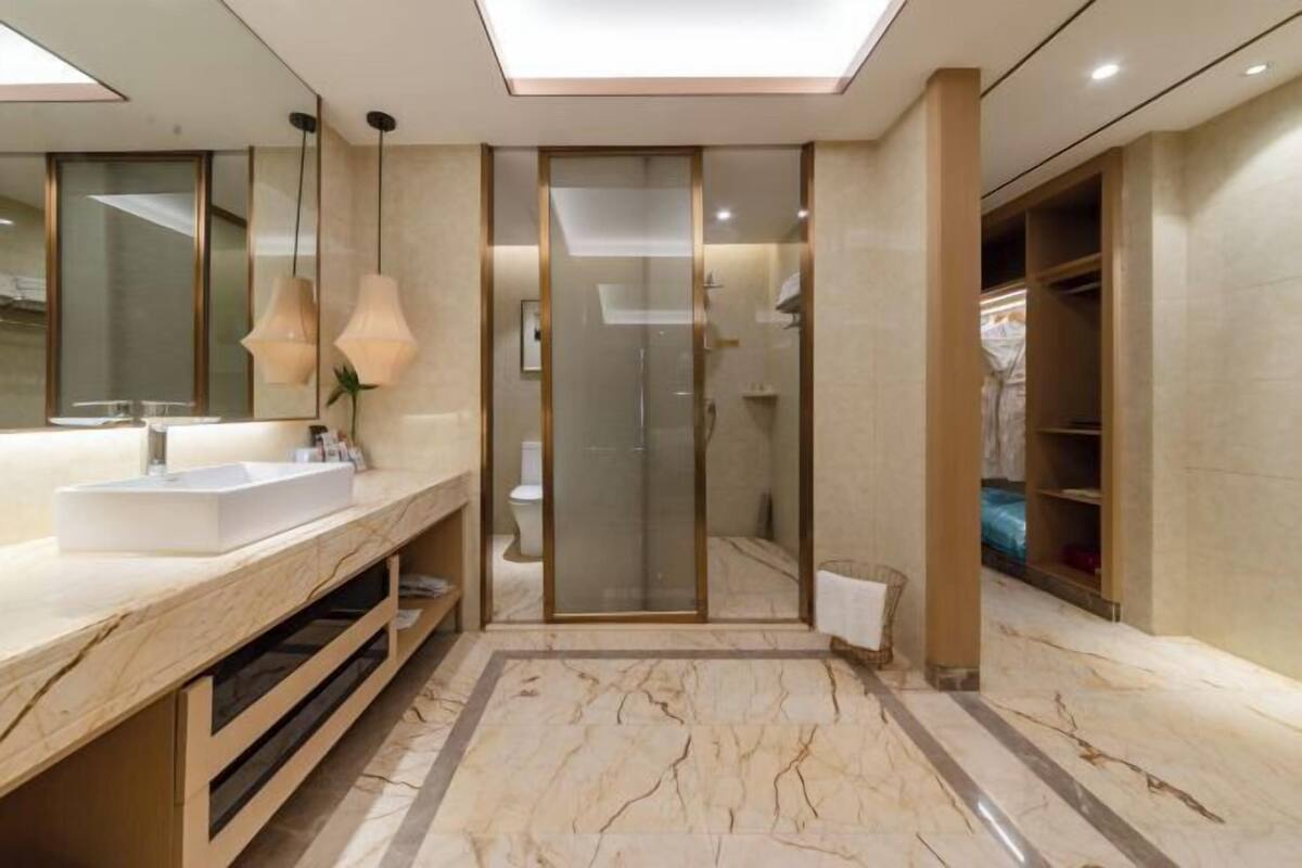 A modern bathroom with a large mirror, a sink, a shower, and a walk-in closet.