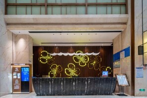 A hotel reception area with a marble reception desk, a digital information kiosk, and a decorative wall with illuminated floral patterns. - Yujingyuan Hotel (Taoyuan)