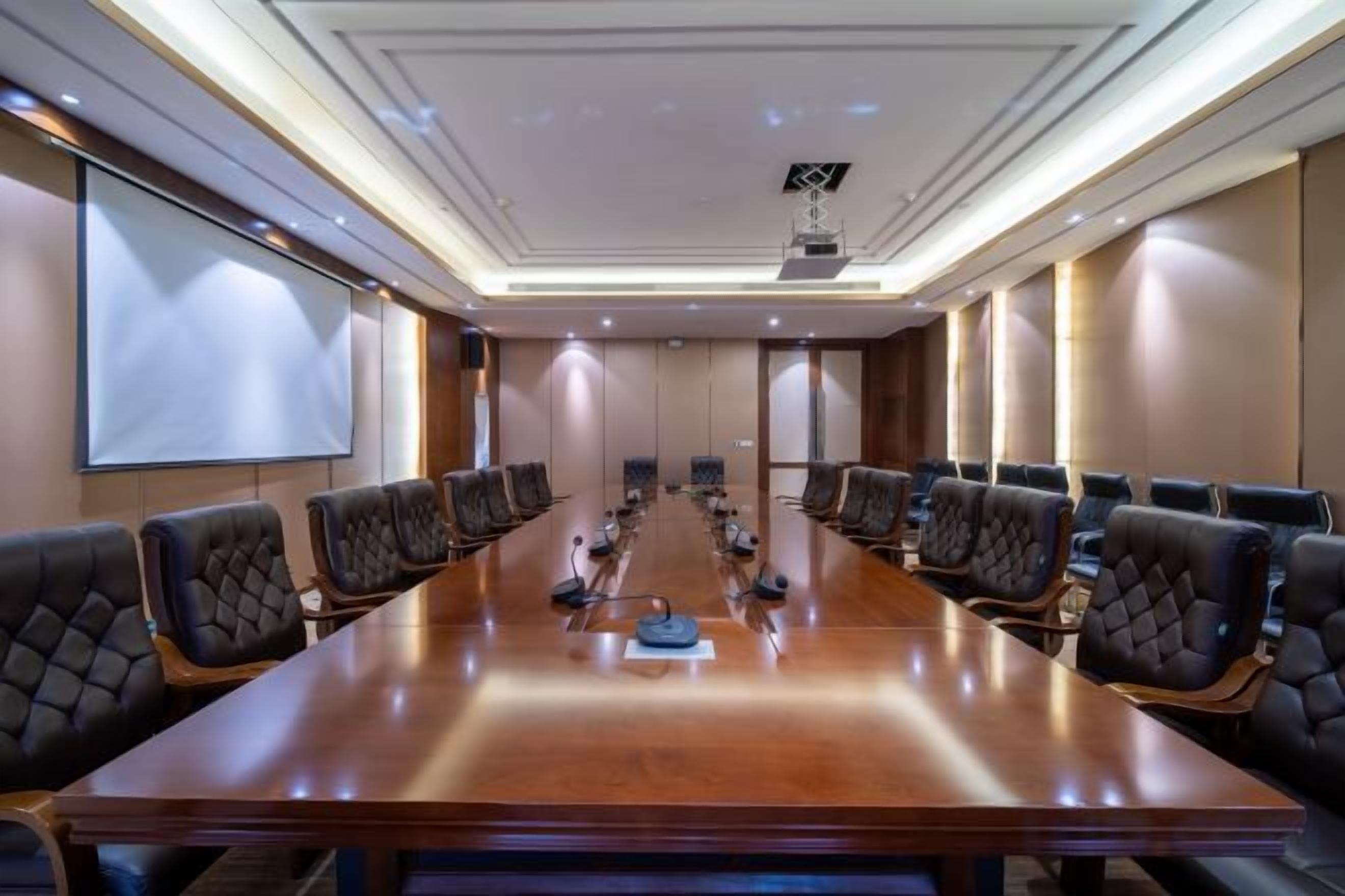 A conference room with a long table and multiple chairs, a projector screen, and a whiteboard.