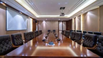 A conference room with a long table and multiple chairs, a projector screen, and a whiteboard.