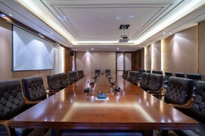 Un salón de conferencias con una larga mesa, varias sillas, una pantalla de proyector y una pizarra.