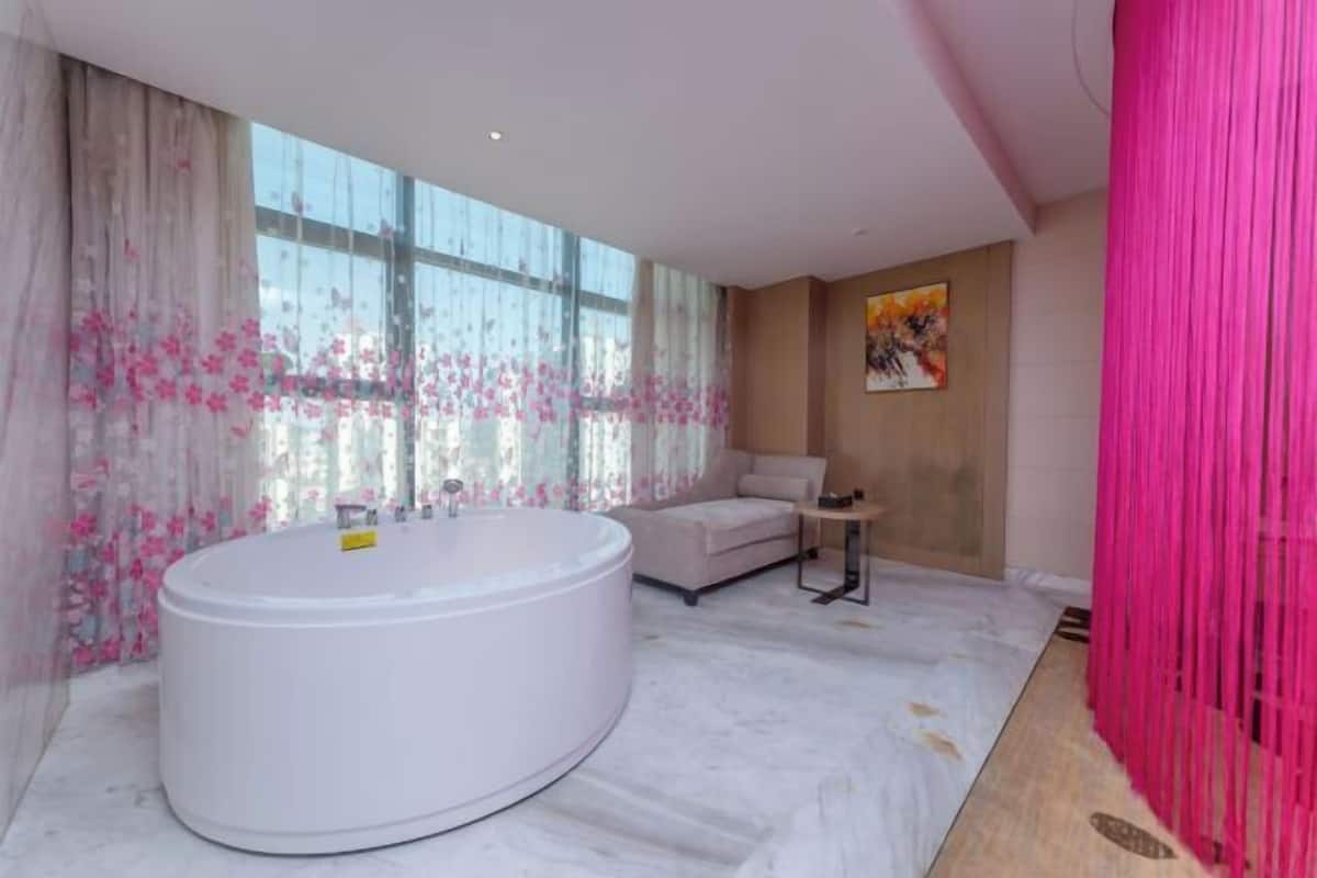 A modern bathroom with a large white bathtub, a sofa, and a small table.