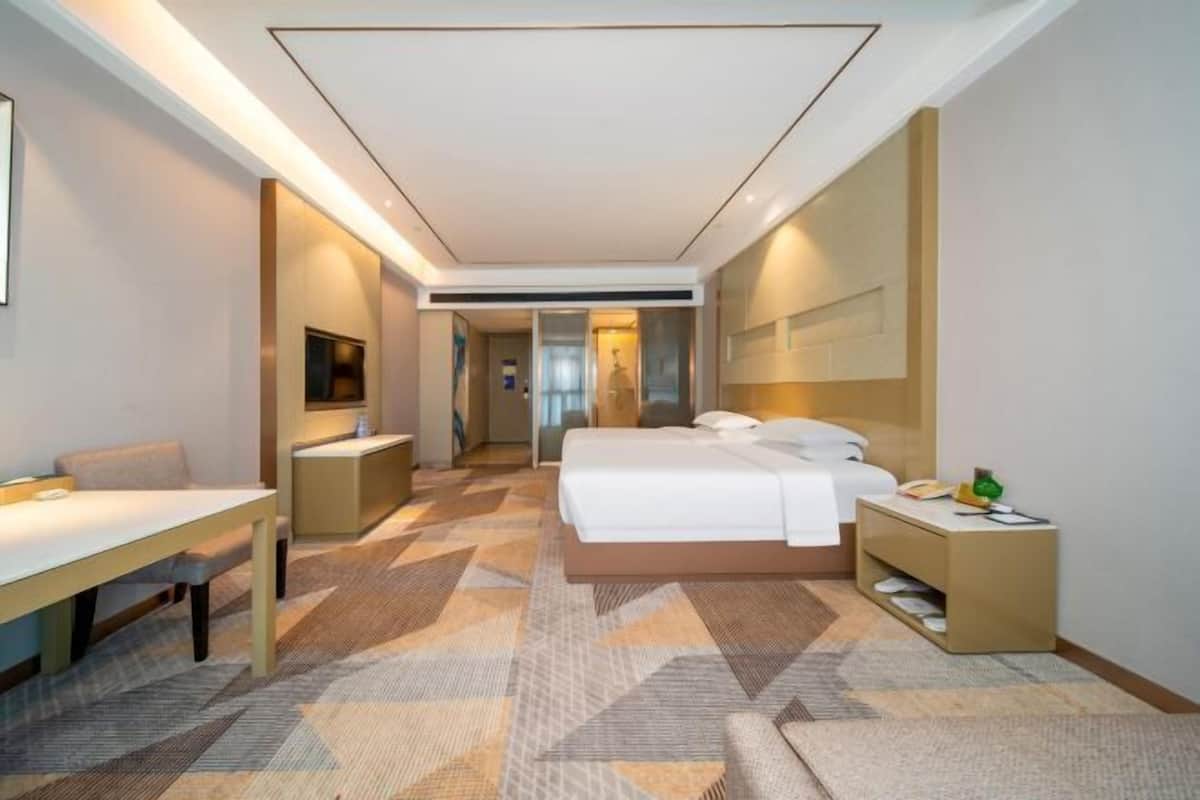A modern hotel room with a bed, bedside table, chair, and a desk.