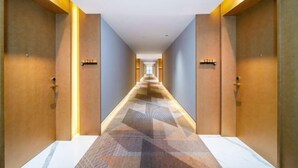 Pasillo de hotel con alfombra de estampado geométrico, puertas de madera e iluminación empotrada.