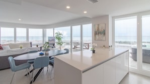 A modern living area with a dining table, chairs, a sofa, and a large window overlooking a cityscape.
