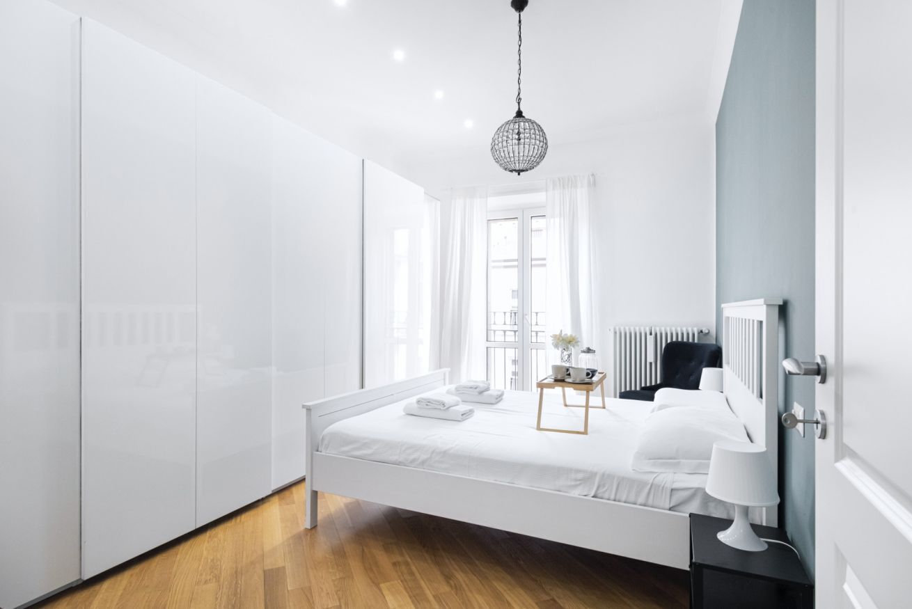 A modern bedroom with a white bed, a bedside table with a lamp, and a hanging light fixture.
