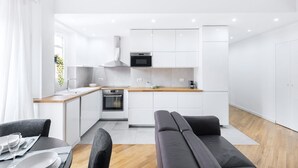 A modern kitchen with white cabinets, a wooden countertop, and stainless steel appliances. There is a dining area with a table and chairs.