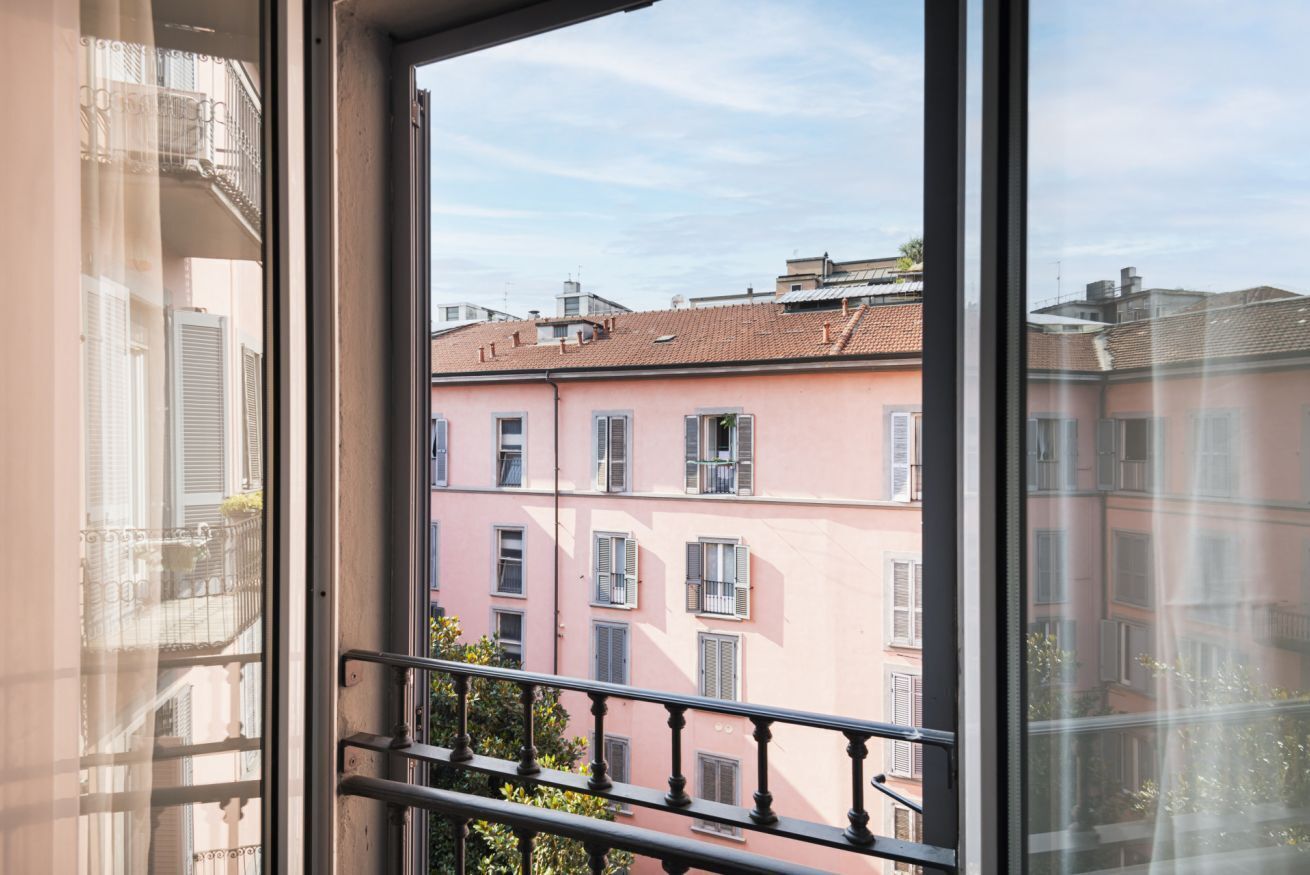 A balcony with a metal railing overlooking a row of pink buildings with shutters.