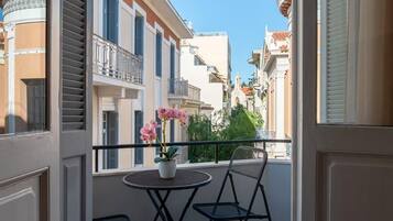 An open balcony with a table and chairs, a potted plant, and a view of a cityscape.