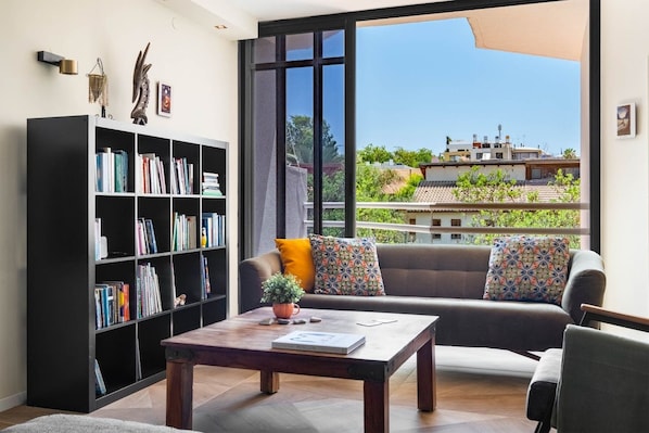 A living room with a large window, a bookshelf, a sofa, and a coffee table.