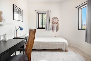A bedroom with a bed, a desk with a lamp, a chair, a dreamcatcher, and a window.