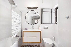 Un bagno moderno con box doccia in vetro, uno specchio rotondo, un lavandino bianco con mobile impiallacciato in legno, un water e un porta asciugamani.