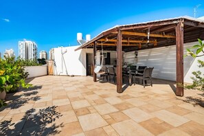 Una terrazza esterna con un pergolato in legno, un tavolo e sedie.