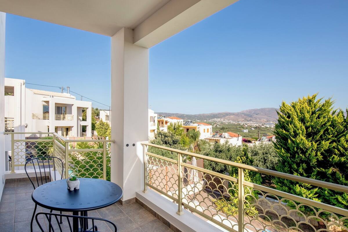 A balcony with a table and chairs, overlooking a residential area with houses and greenery.