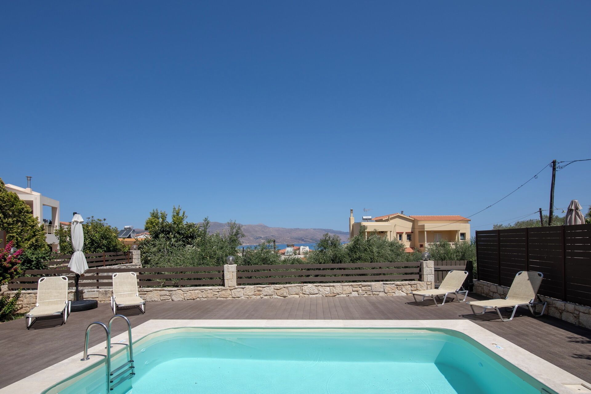 Una piscina con lettini e vista su edifici e montagne sullo sfondo.