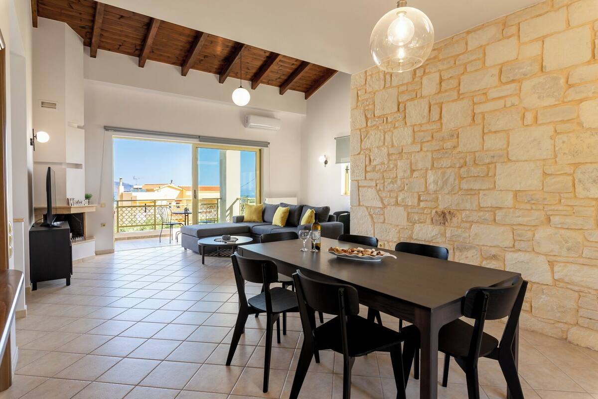 A spacious living area with a stone wall, a dining table with chairs, and a sofa with cushions.