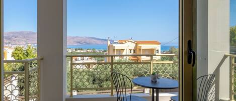 A balcony with a table and chairs, offering a view of a coastal town and mountains.