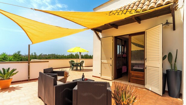 Um terraço com móveis de vime, uma cobertura amarela e plantas em vasos.