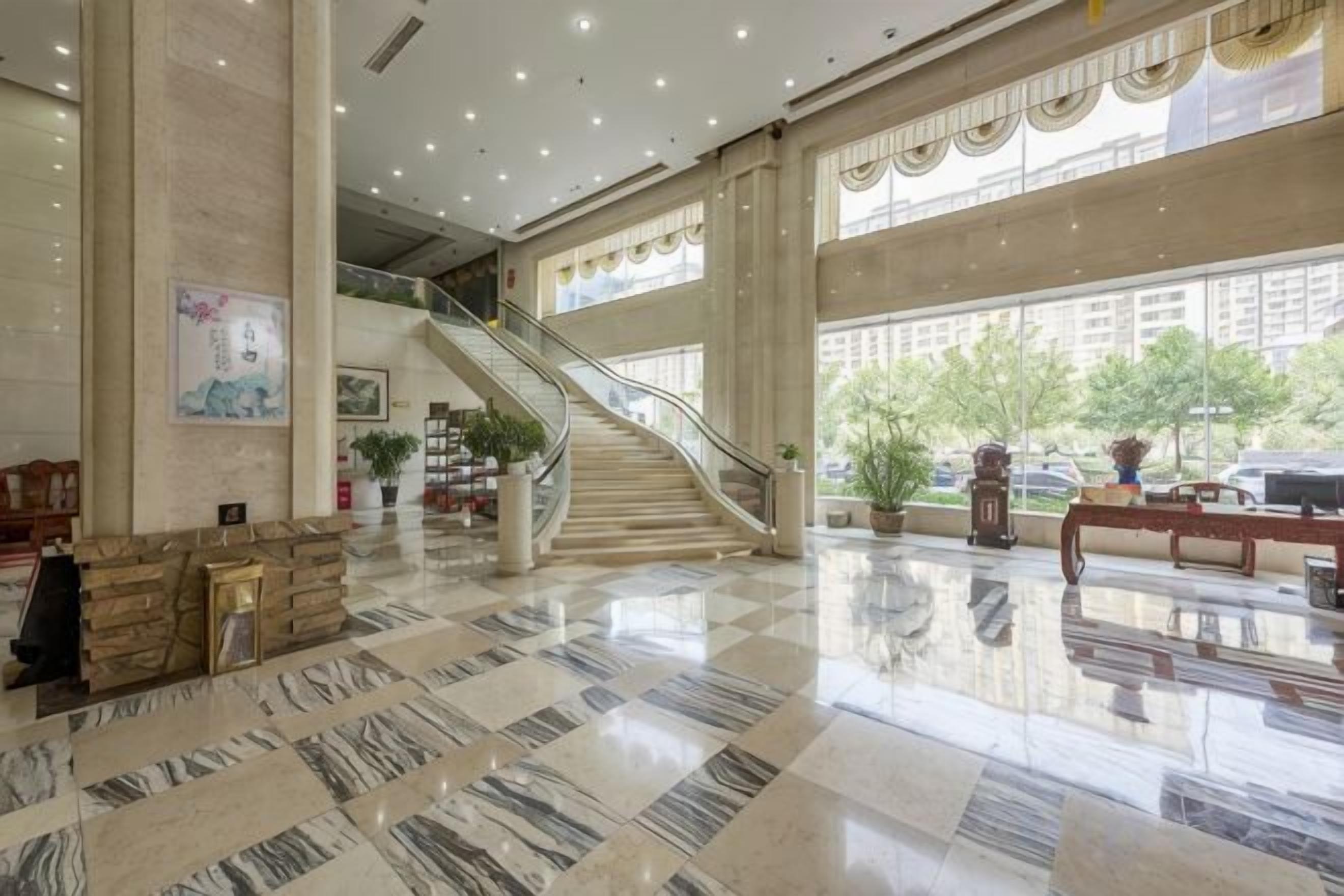 A spacious lobby with a marble floor, a staircase, and large windows.