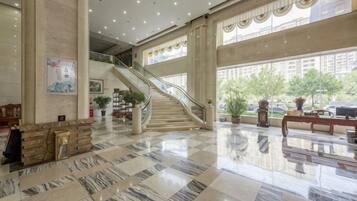 A spacious lobby with a marble floor, a staircase, and large windows.