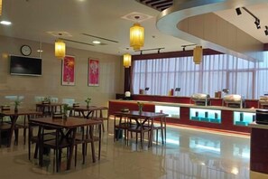Un restaurante con mesas y sillas de madera, una barra con exhibición de alimentos y faroles colgantes.