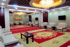 Un hall d’hôtel avec un tapis rouge, un espace salon et un téléviseur fixé au mur.