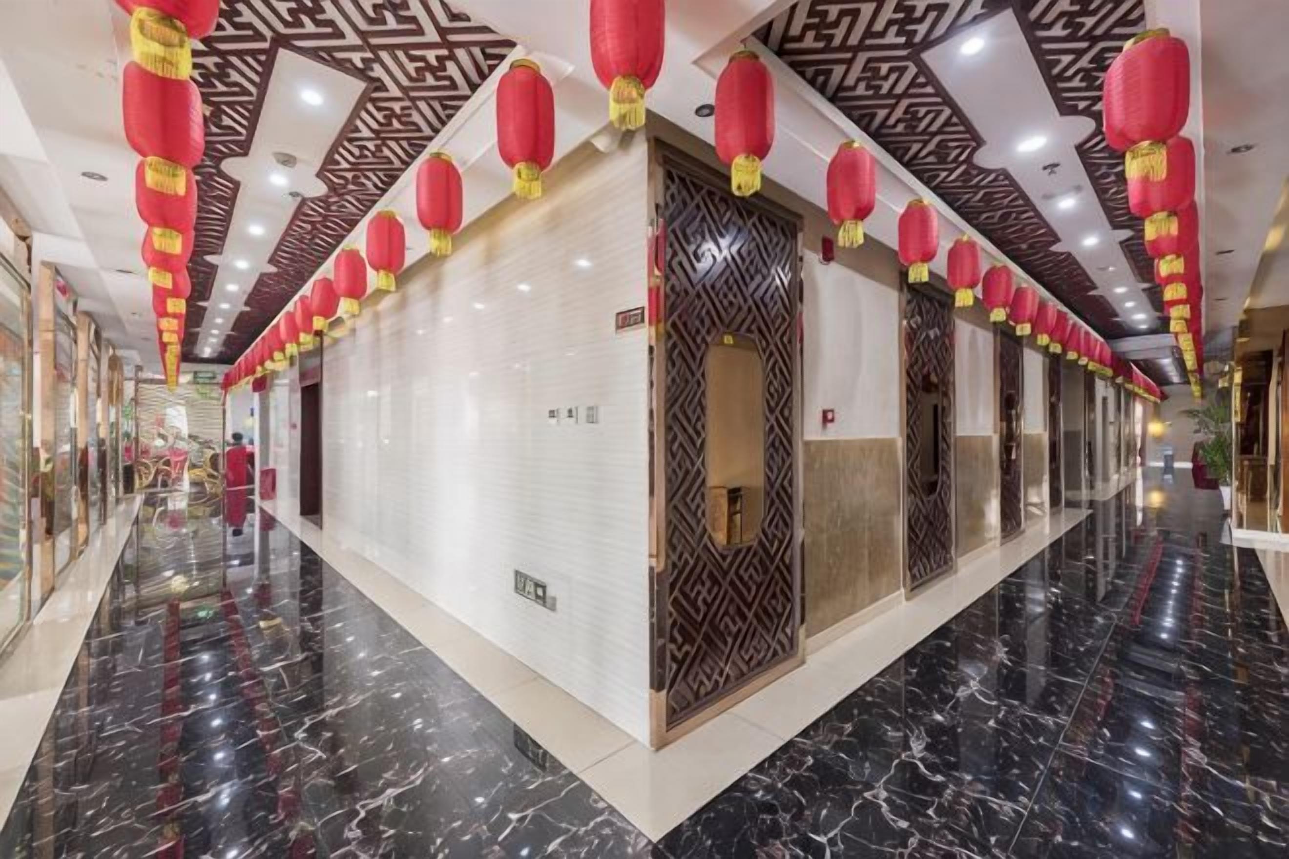 A hotel corridor with a polished marble floor, patterned ceiling, and red lanterns.