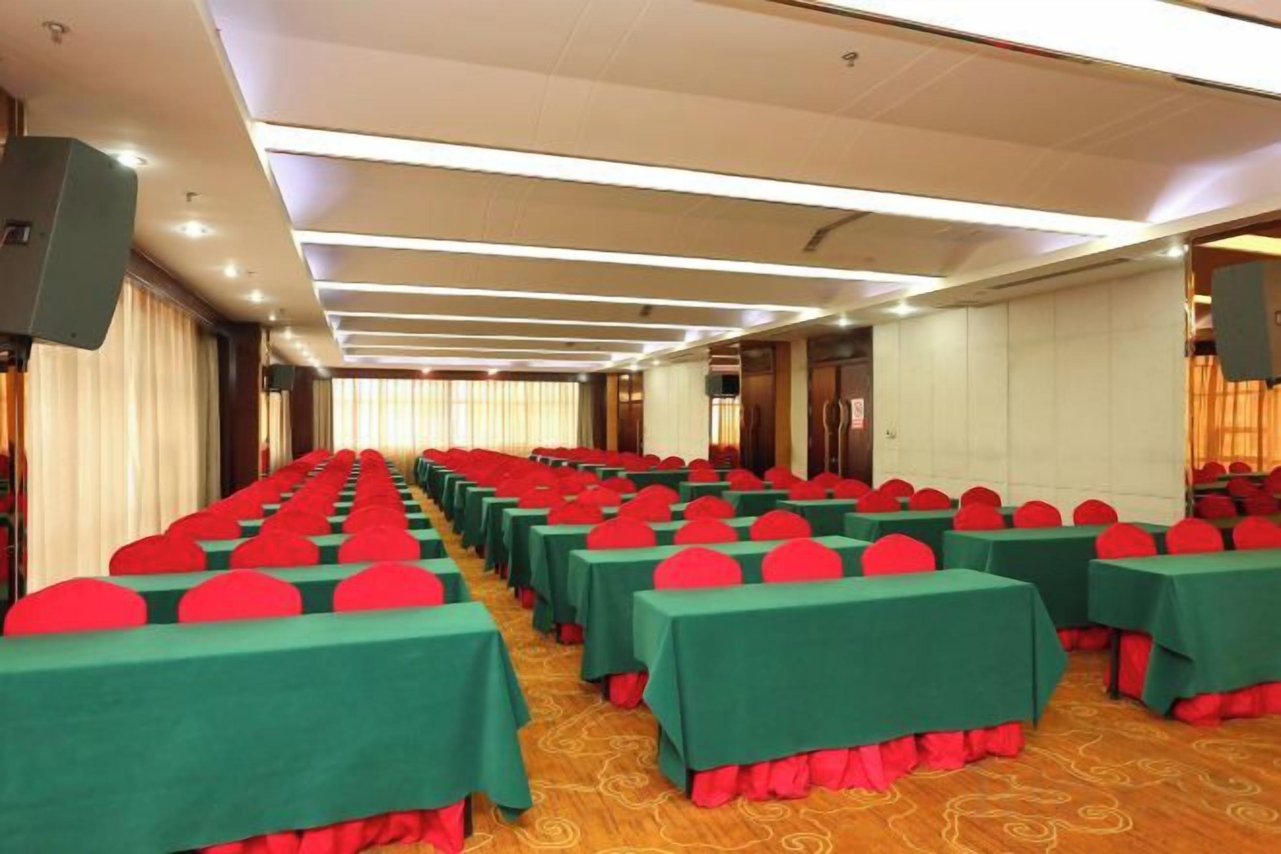 A conference room with rows of tables, each with a green tablecloth and red chair cushions.