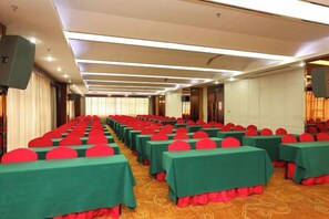 Un salón de conferencias con filas de mesas, cada una con mantel verde y cojines rojos.