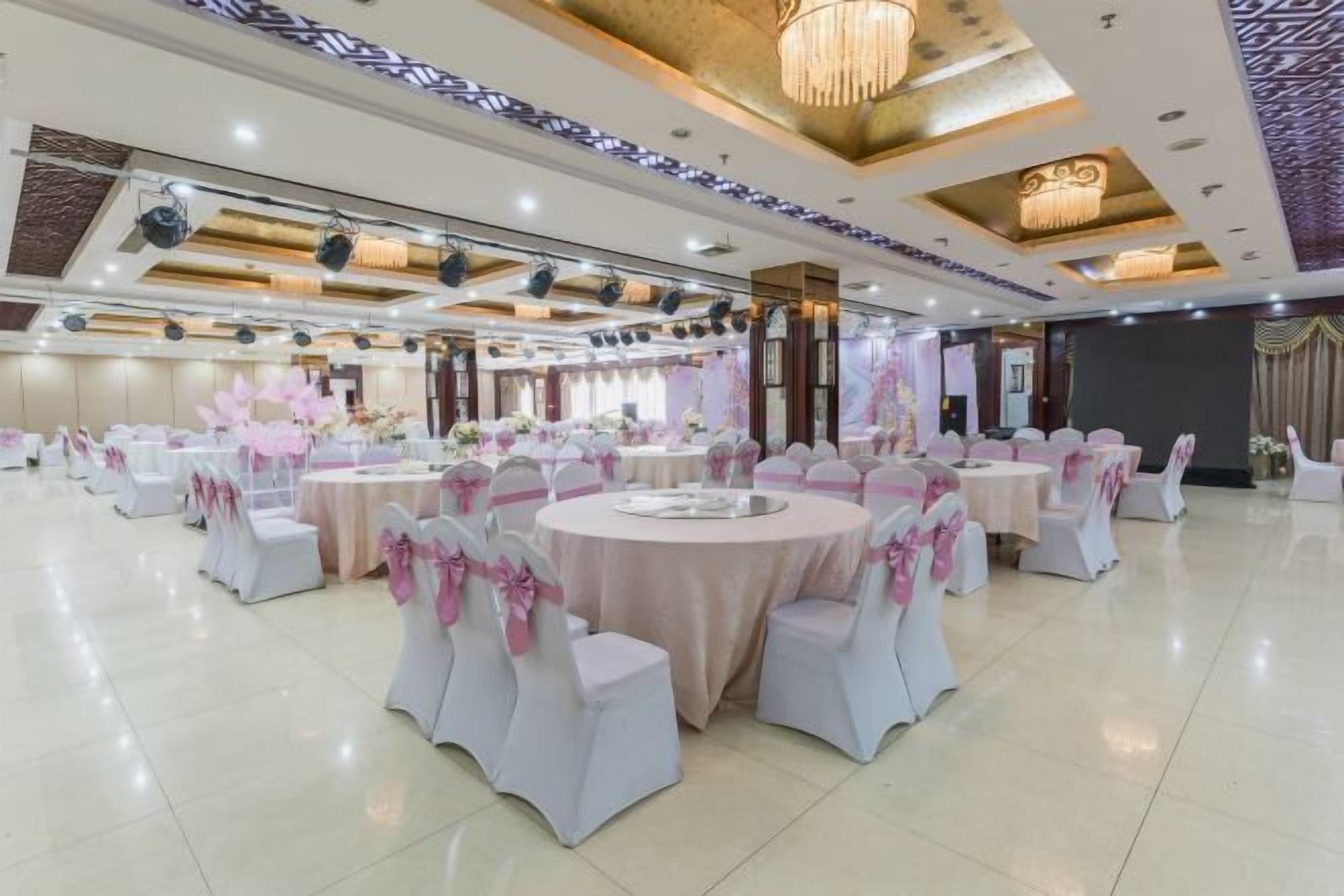 A banquet hall with round tables and white chairs, each with pink sashes.