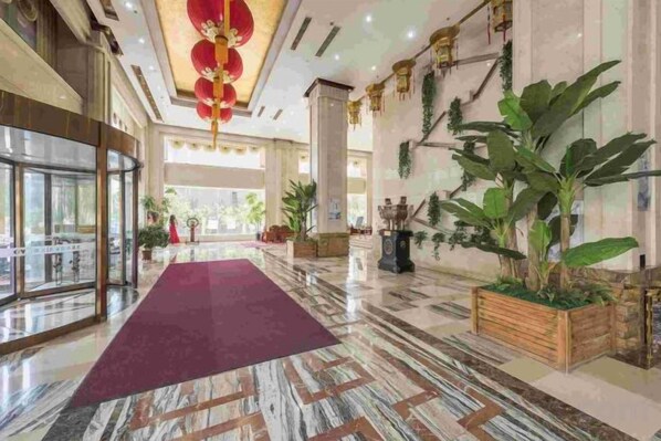 Un vestíbulo de hotel con piso de mármol, alfombra roja y grandes plantas en macetas.