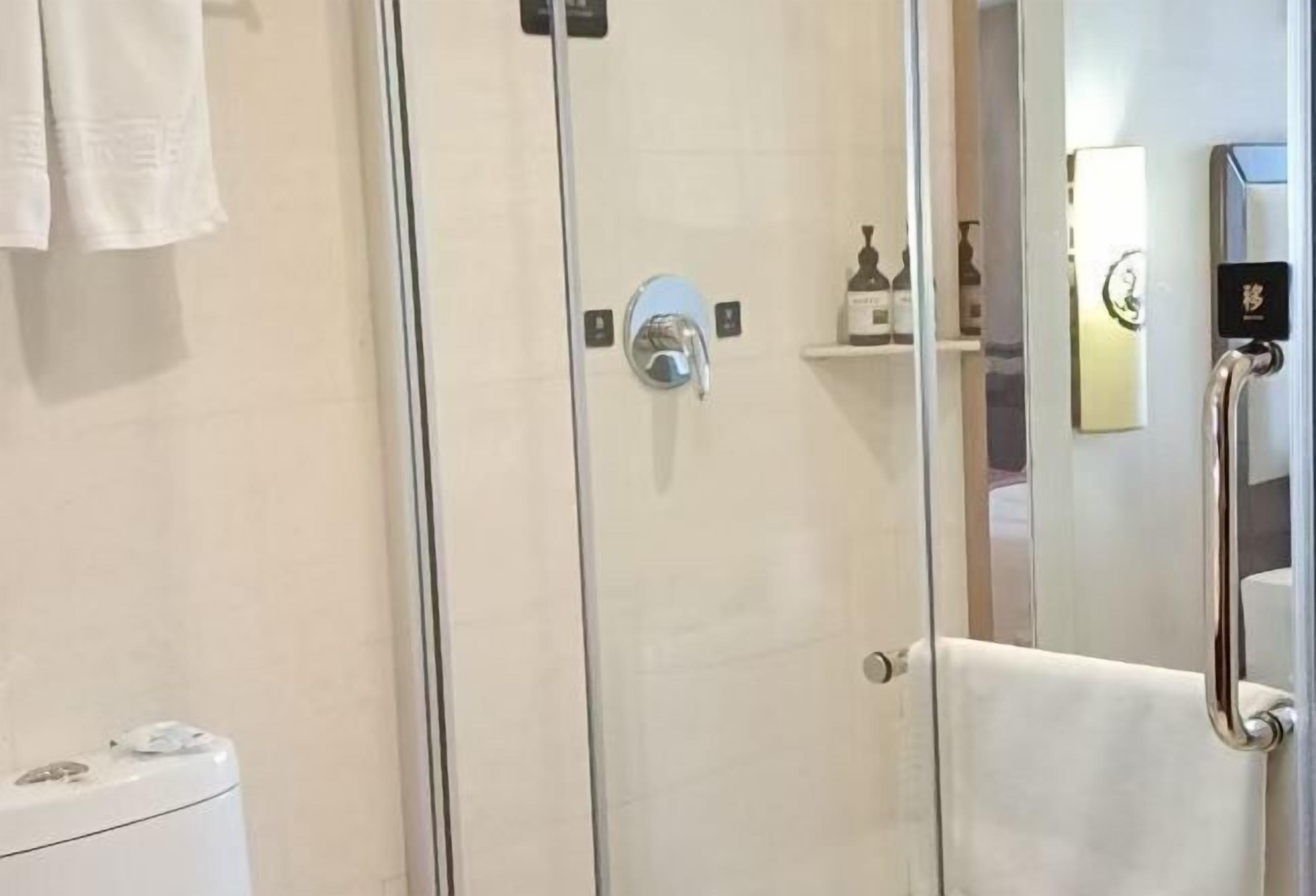 A glass-enclosed shower with a handheld showerhead, a white towel hanging on a rack, and a small shelf with toiletries.
