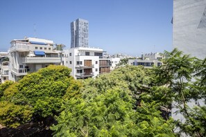 A modern urban landscape with multi-story buildings, including a prominent skyscraper, surrounded by lush greenery. - Green Oasis in Tel Aviv's Old North by SeaNRent (Tel Aviv)