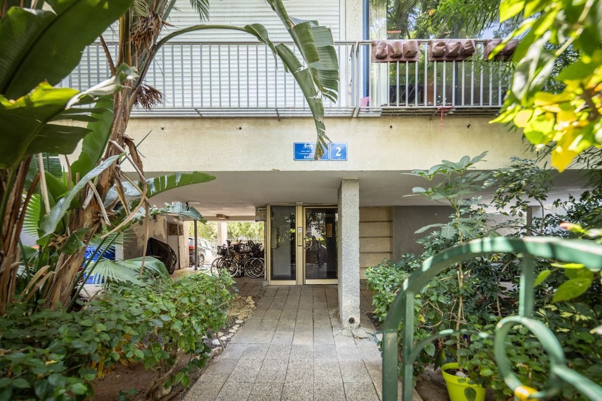 A covered outdoor area with a building entrance, a bicycle parked outside, and lush greenery.