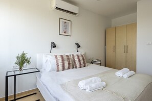 Een hotelkamer met een bed, nachtkastje met een lamp, een kledingkast en een ingelijst schilderij aan de muur.