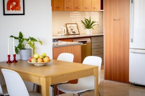 A modern kitchen with wooden cabinets, a white countertop, and a dining area with a wooden table and white chairs. - Green Oasis in Tel Aviv's Old North by SeaNRent (Tel Aviv)